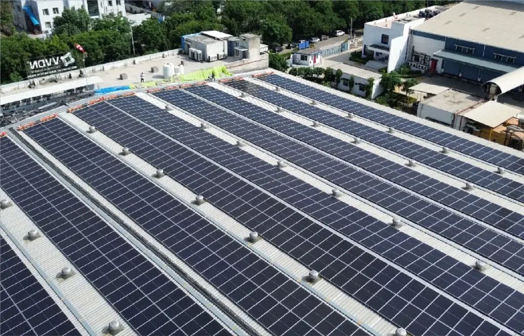 Aerial view of a large commercial factory roof covered in long rows of solar panels